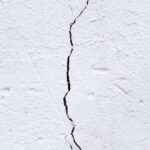 Textured background of rough uneven surface with cracks and scratches on white wall