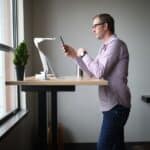 man in pink dress shirt and blue denim jeans standing beside brown wooden table