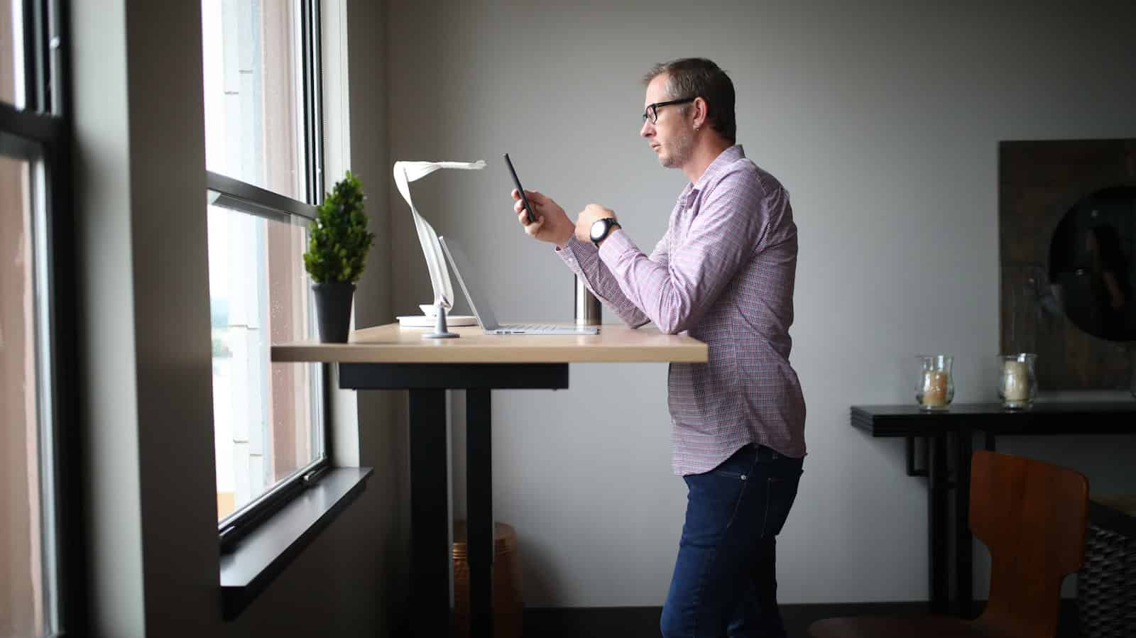 man in pink dress shirt and blue denim jeans standing beside brown wooden table