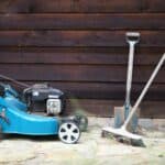 green and black push lawn mower beside brown wooden wall